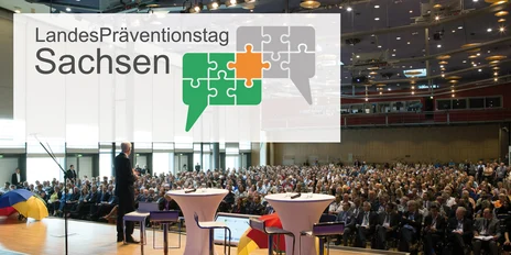 ein mit Menschen auf Stühlen sitzend großer Saal mit weißen Stehtischen im Vordergrund. Auf diesem Bild ist das Logo vom Landespräventionstag mit Sprechblasen die Puzzlestücke zeigen dargestellt