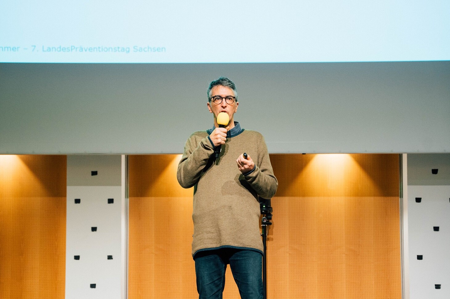 Mario Tormo Romero spricht auf der Bühne mit einem Mikrofon in der Hand und vor einer Leinwand