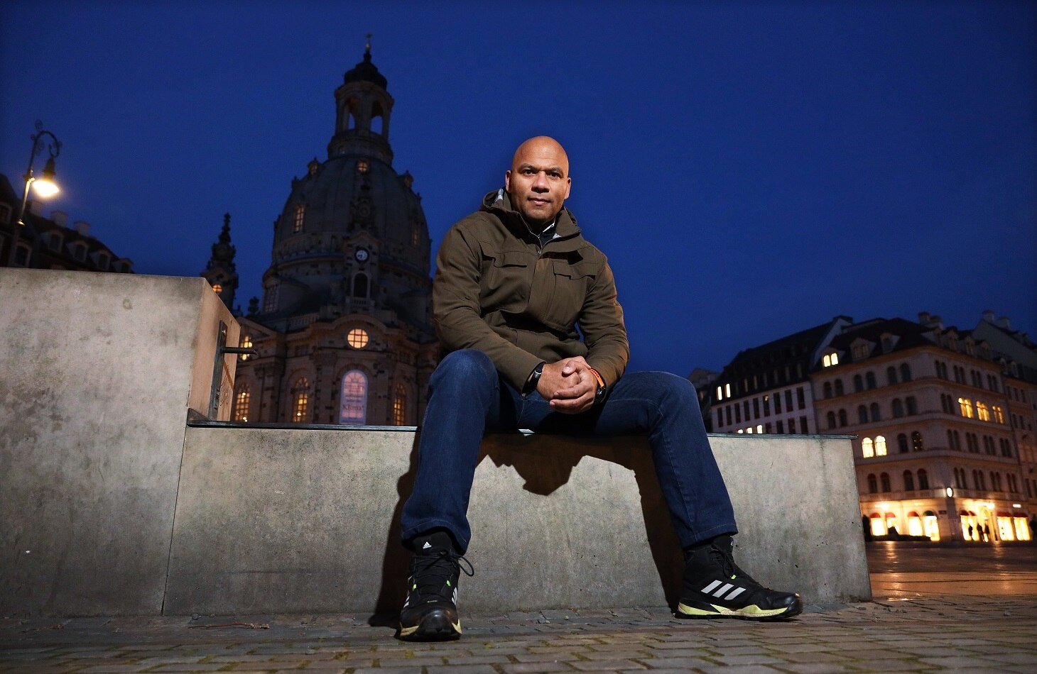 Samuel Meffire sitzend auf einer Mauer, dahinter die Siluette der Frauenkirche in Dresden